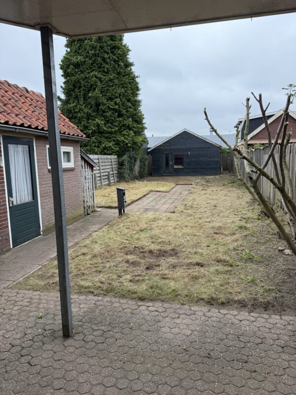 Tuin in Almelo ná het tuinonderhoud door CleanNL, gezien vanaf het terras — gemaaid gazon en vrij tuinpad naar het tuinhuis
